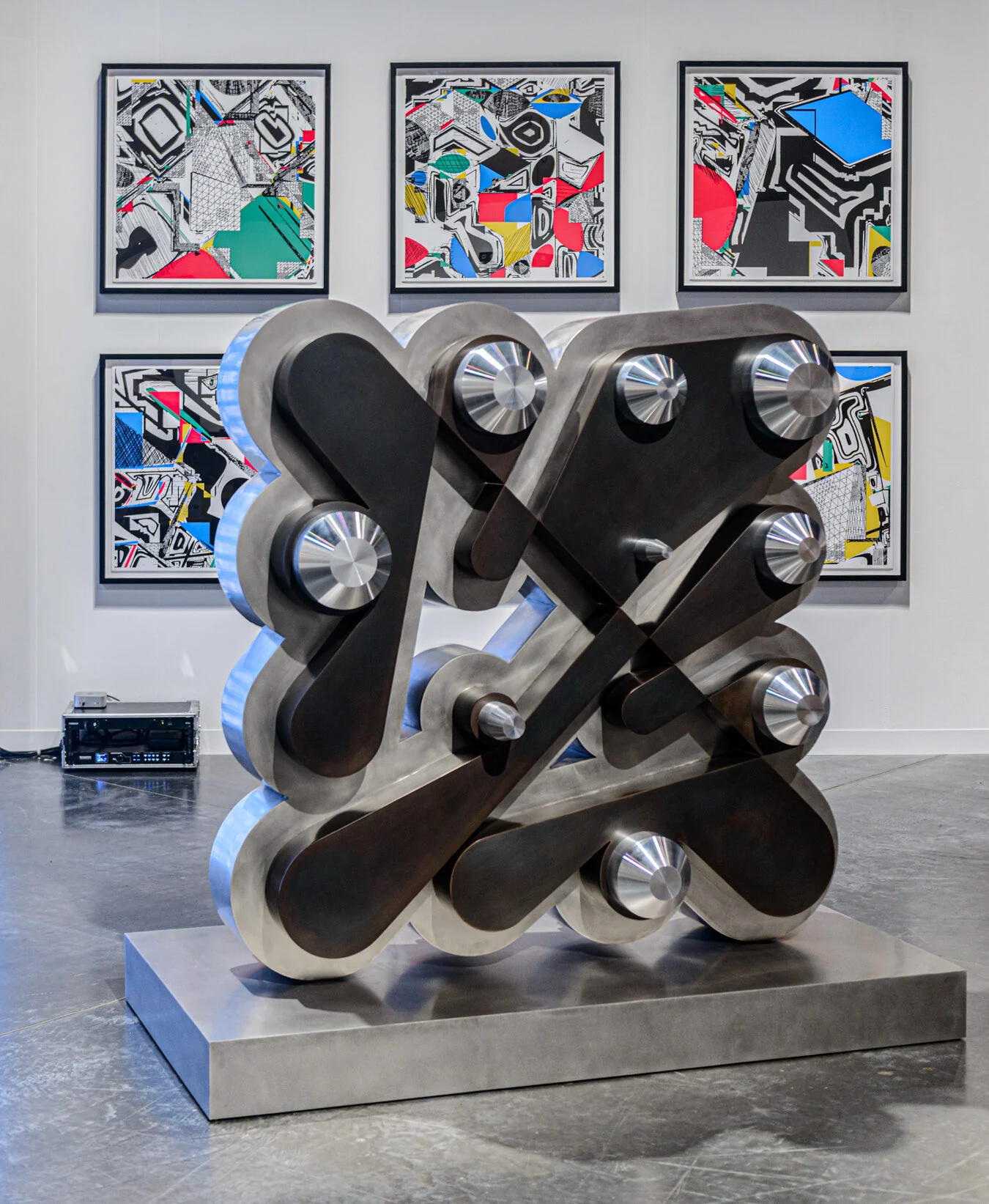 Floor Ringer, a freestanding metal sculpture with cylindrical pegs, in front of Polygon Etcetera prints.