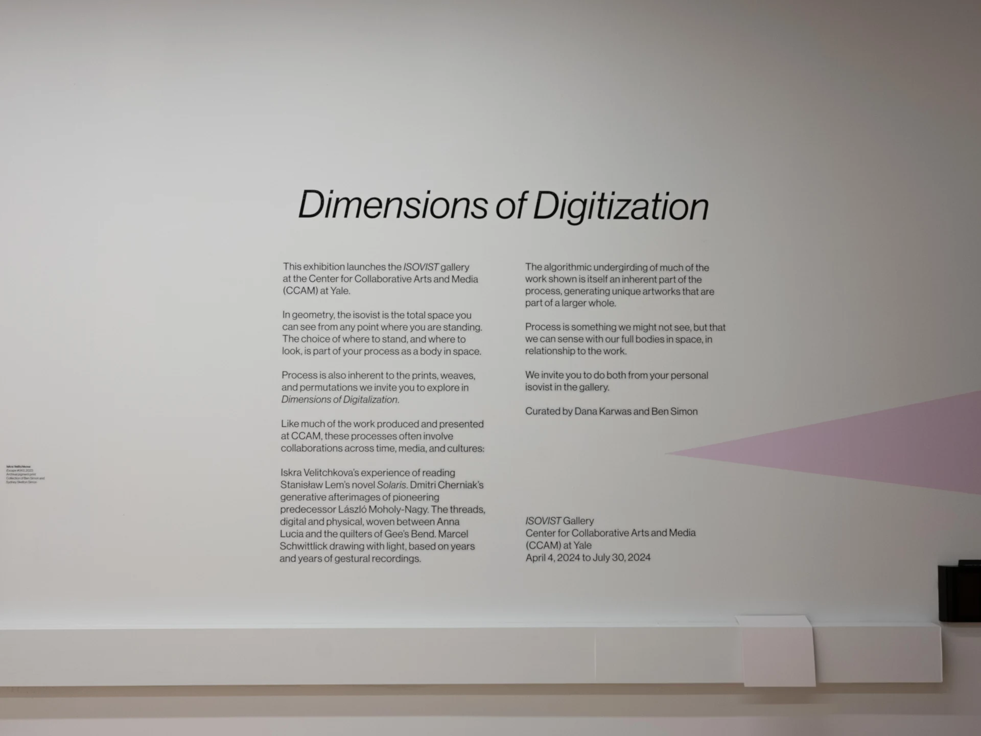 A white wall with the title Dimensions of Digitization in black italic type above two columns of exhibition text, with a pale pink triangle at right.