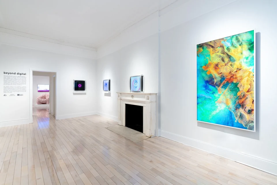 A white gallery room with a marble mantelpiece; A breath of fresh pearls glows in a clear acrylic case on the mantel, beside a large vertical screen.