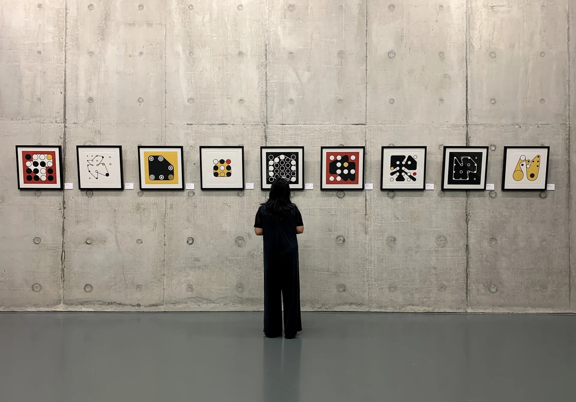 A visitor looking at nine framed Ringers prints arranged across a concrete gallery wall.