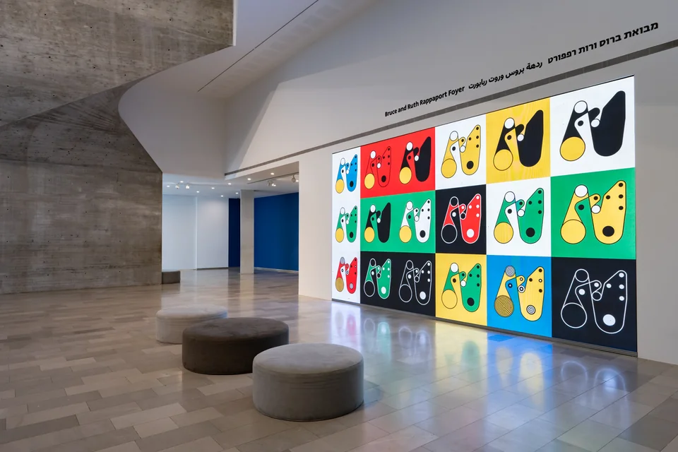 An angled view of fifteen colorful Ringers compositions beside the concrete museum stairwell.