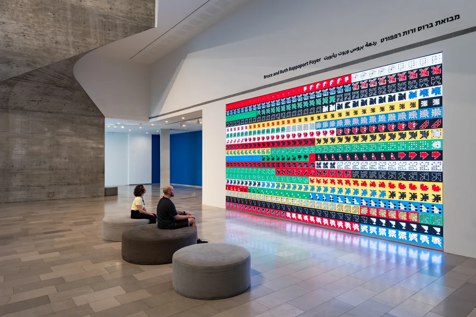 Two people seated before a wall-sized grid of colorful Ringers in the museum foyer.