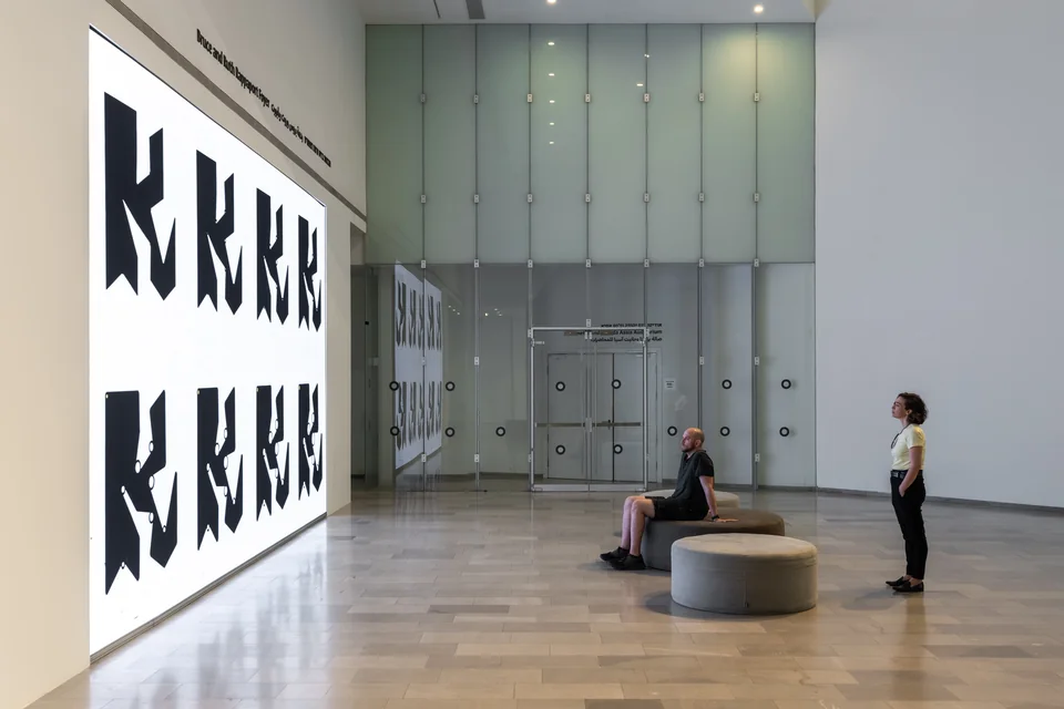 Two people viewing large black Ringers on a white screen, reflected in the glass wall.