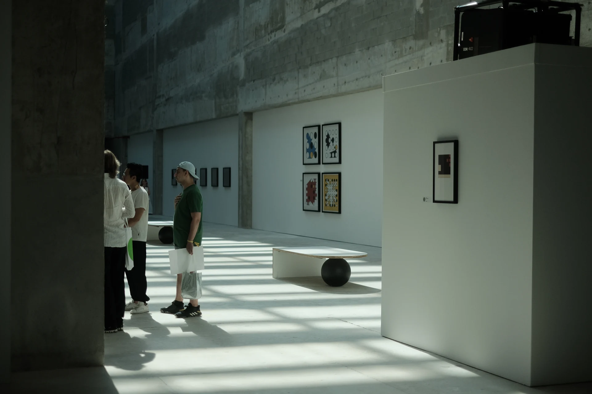 Visitors in the gallery, with four framed Ringers on the wall beyond a concrete column.