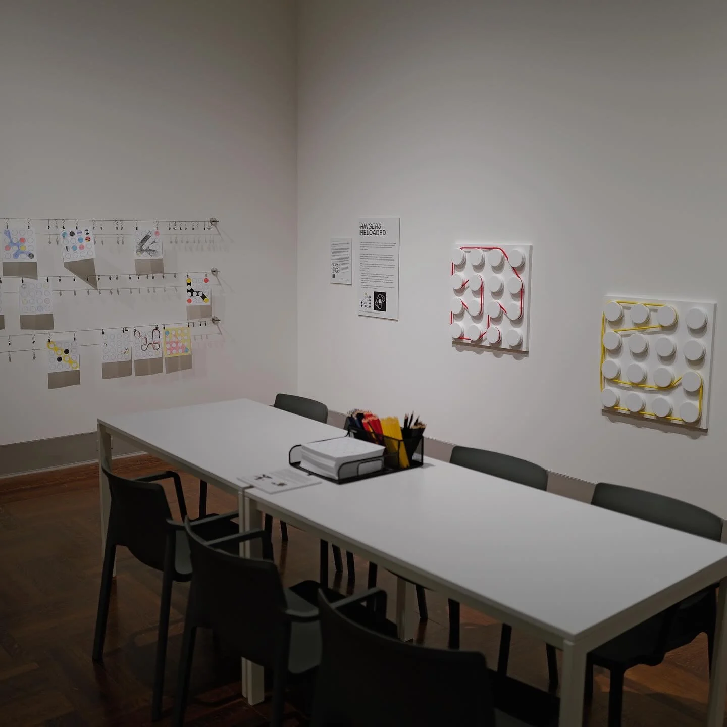 Pencils and paper on a table in the Ringers Reloaded activity area, with drawings and peg boards on the walls.