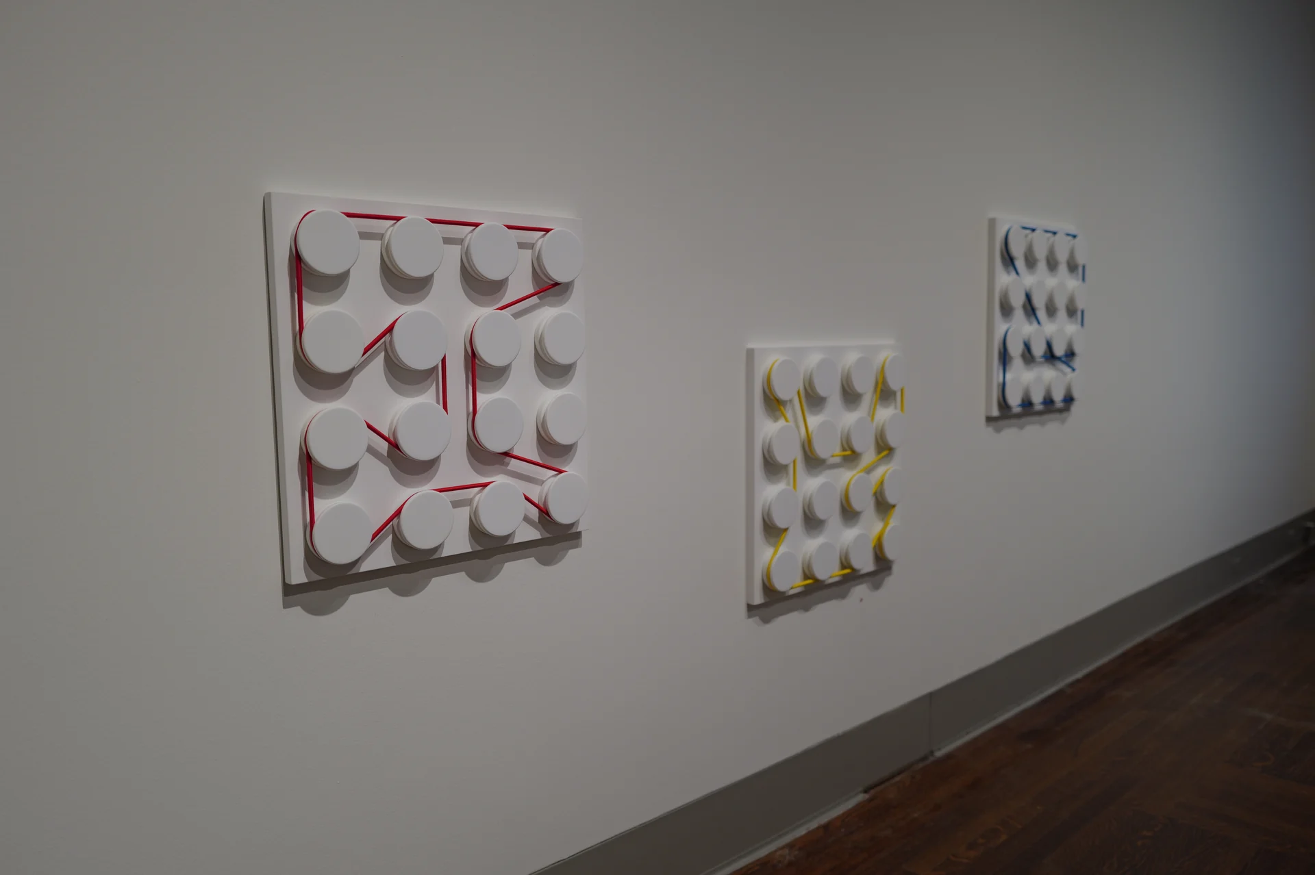 Three white peg boards with red, yellow, and blue strings wrapped around circular pegs.