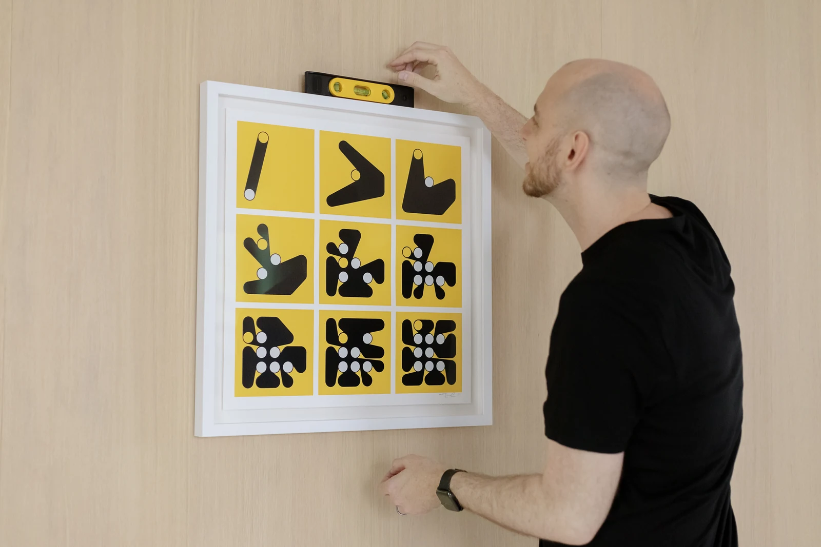 Dmitri Cherniak positioning a framed LACMA Iterations print on a wall.
