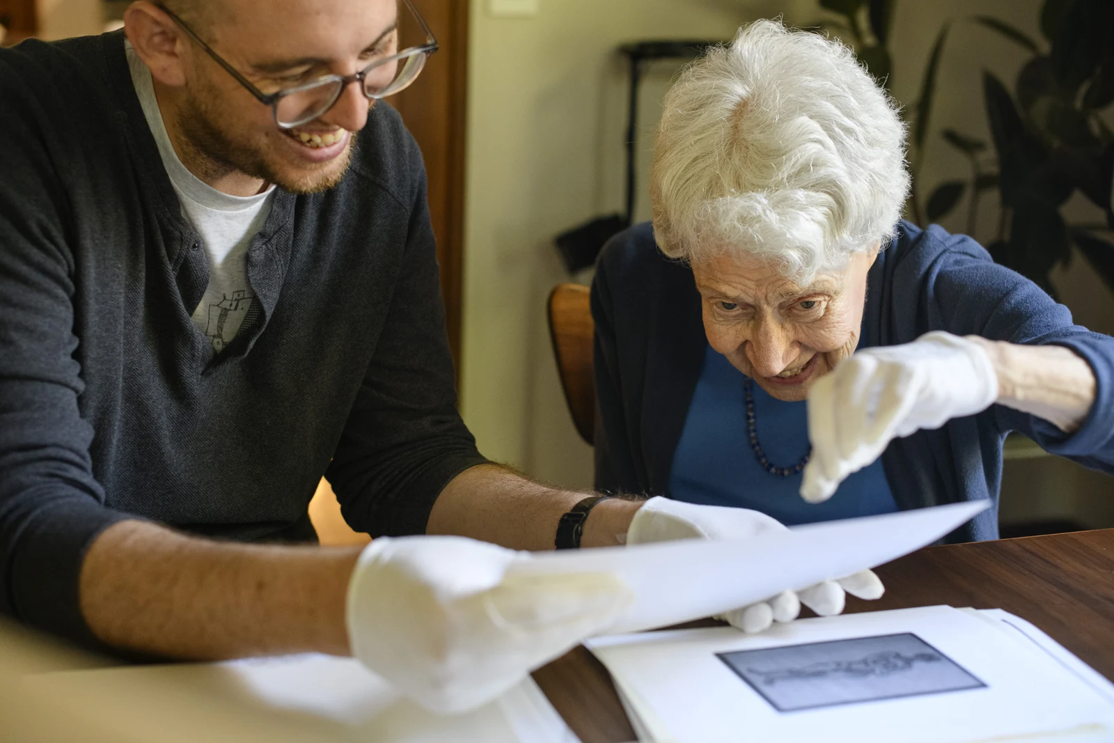 Dmitri Cherniak and Hattula Moholy-Nagy wearing white gloves and looking at an artwork in the László Moholy-Nagy archive in Ann Arbor, Michigan.