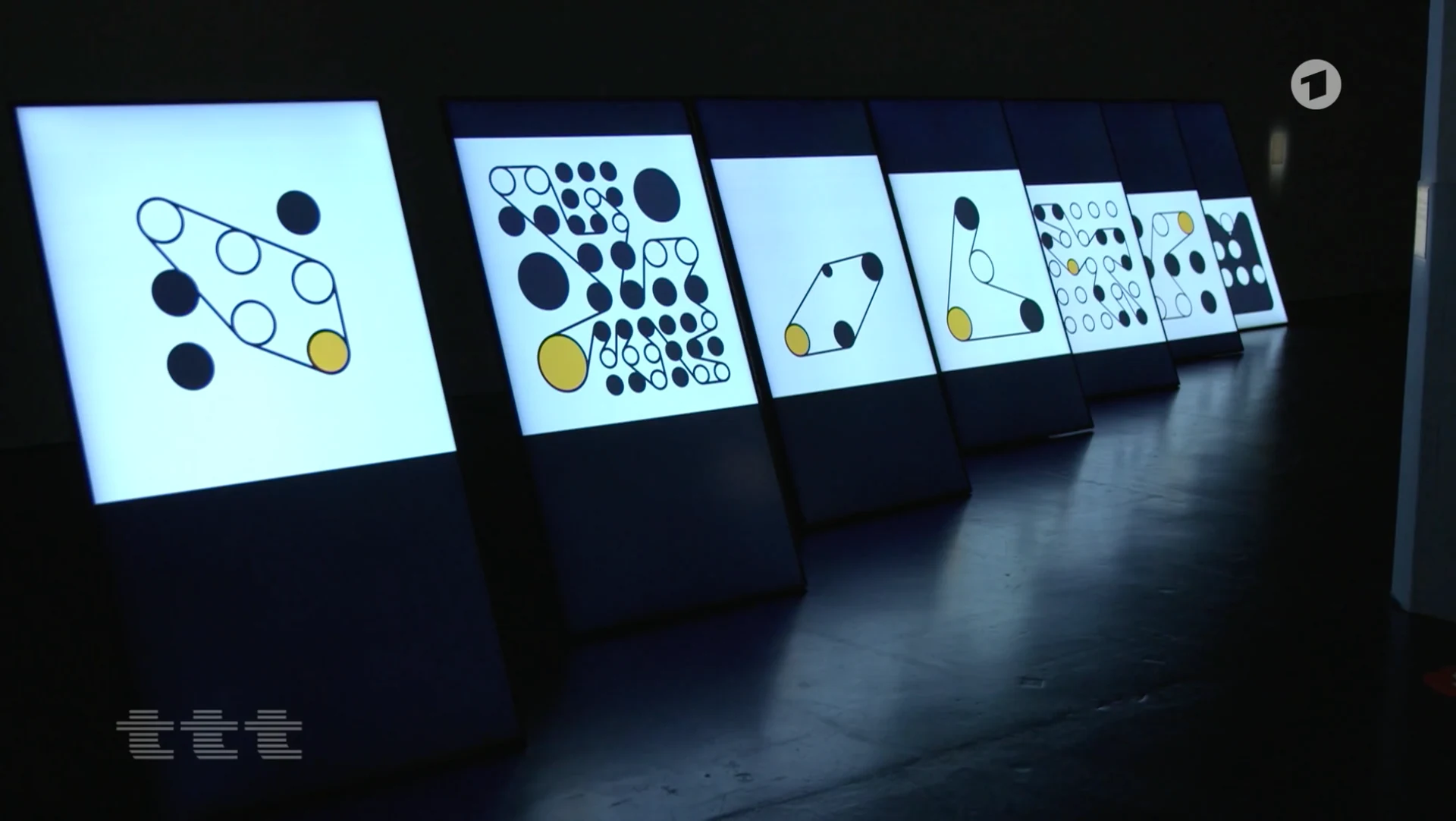 A row of freestanding screens at ZKM showing Ringers with outlined strings and black, white, and yellow pegs.
